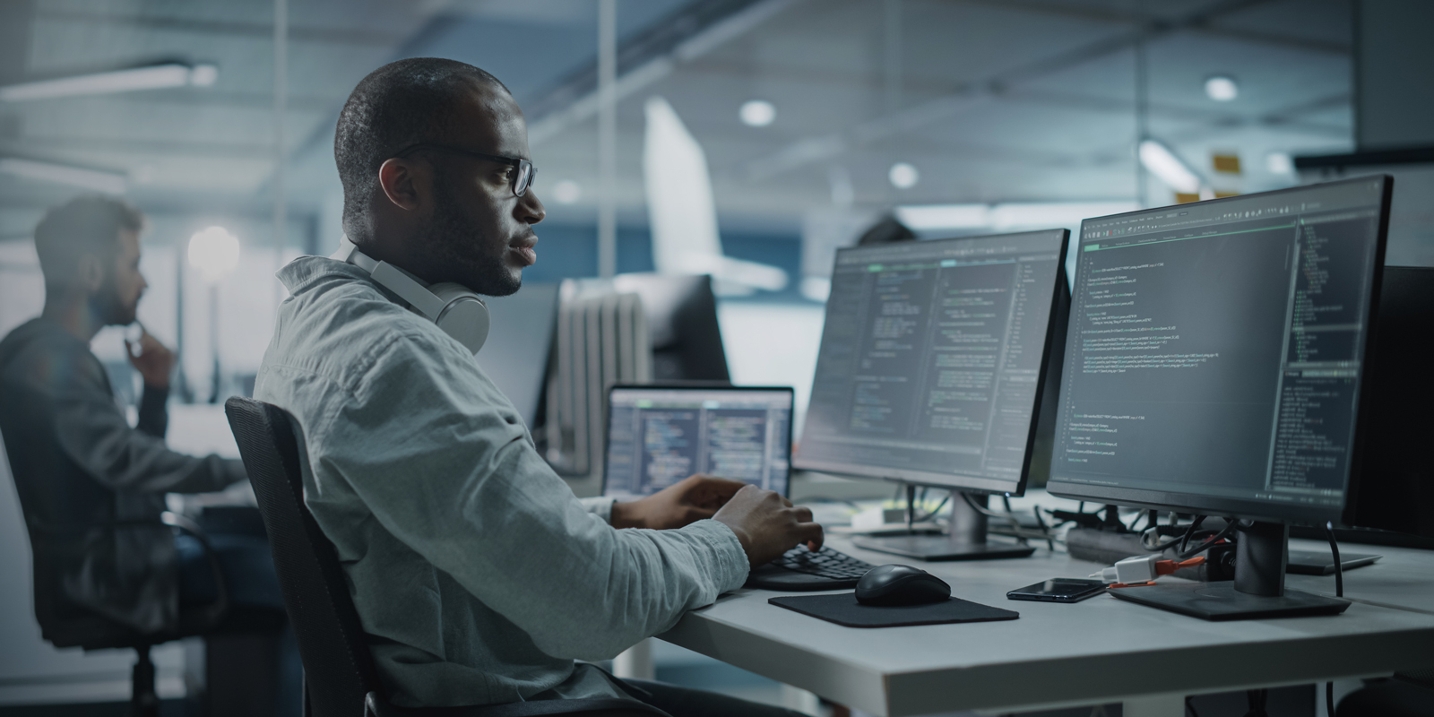 person with three screens on their desk looks at rows of code